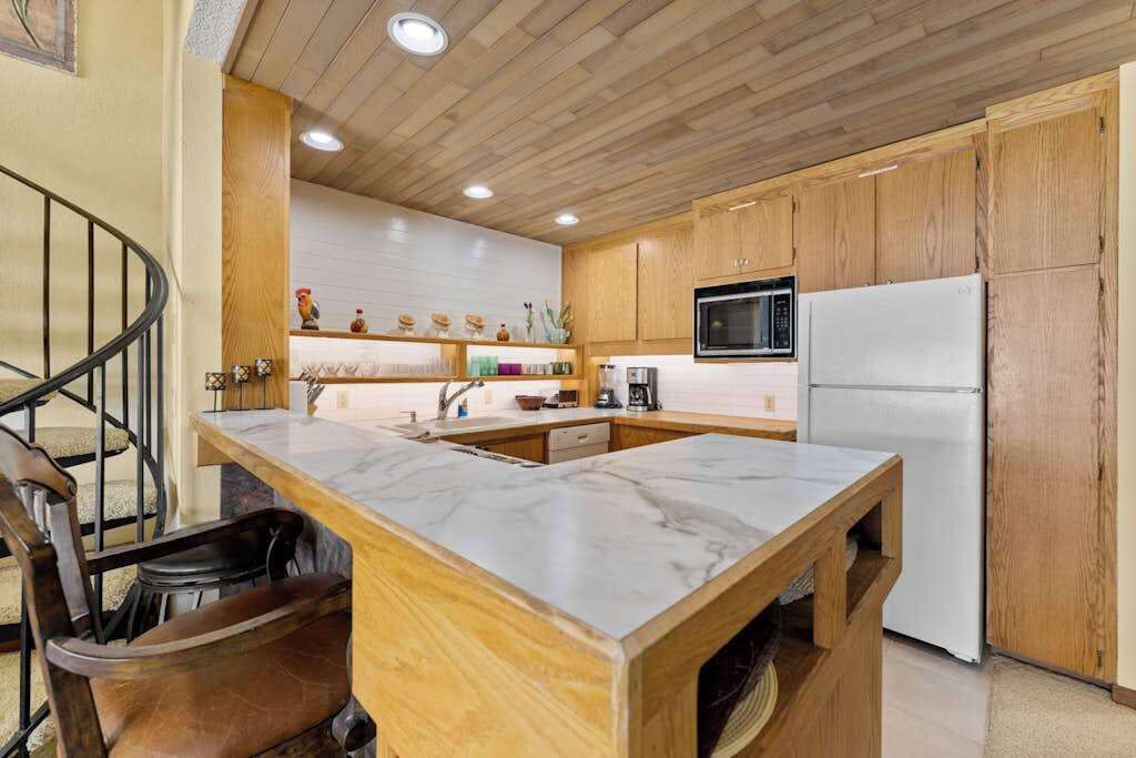 Une cuisine avec des meubles en bois, un plan de travail en marbre, un réfrigérateur blanc et un four à micro-ondes.