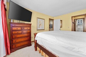 Ein Schlafzimmer mit einem Bett, einem Schminktisch, einem Fernseher und einer Tür zu einem anderen Raum.