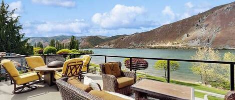 Una terraza con mobiliario de mimbre y vistas a un lago y colinas.