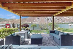 A covered outdoor seating area with wicker furniture and a view of a lake and mountains. - 4BR dog friendly waterfront home with shared pool (Orondo)