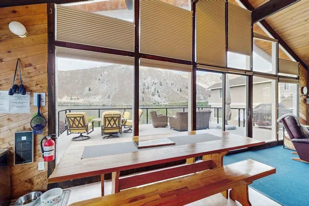 A wooden interior with a large table and chairs, a fire extinguisher, and a view of mountains through large windows.