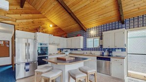 Een keuken met houten balken in het plafond, witte kasten, een centraal eiland met krukken en een blauwe tegelachtergrond.