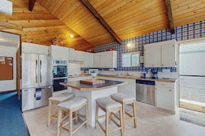A kitchen with wooden ceiling beams, white cabinets, a central island with stools, and a blue-tiled backsplash. - 4BR dog friendly waterfront home with shared pool (Orondo)