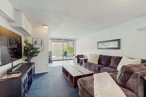 A modern living room with a sofa set, a coffee table, a flat-screen TV, and a large window.