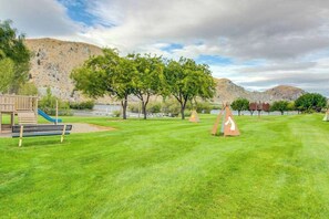A grassy outdoor area with a playground, trees, and a mountain in the background.