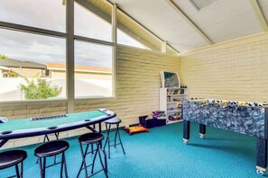 A room with a foosball table, pool table, and bar stools.