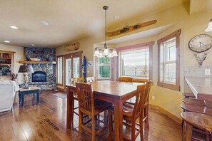 A spacious dining area with a large wooden table and chairs, a stone fireplace, and a view of the outdoors through large windows. - 4BR Lakeview - Fireplace - Deck - W&D (Chelan)