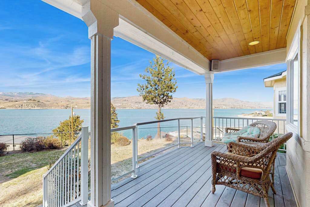 A covered porch with a view of a lake and mountains.