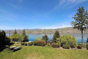 Uma área ajardinada com piscina, árvores e vista para um lago e montanhas.