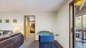 Una habitación con mesa de fútbol de mesa, un sofá de cuero marrón y una puerta de cristal que da a un espacio exterior.
