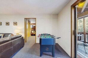 Ein Zimmer mit einem Kicker, einem braunen Ledersofa und einer Glastür zu einem Außenbereich.
