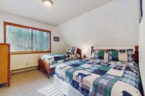 A bedroom with two beds, a window, and a small bedside table.