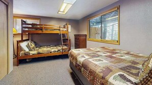 Una habitación con literas, cómoda, ventana con persianas y una lámpara en el techo.