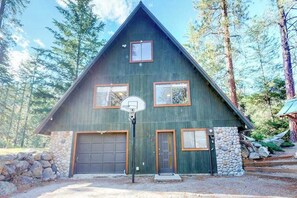 A two-story cabin with a stone foundation, two garage doors, and a basketball hoop in front.