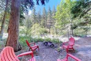 Ein bewaldetes Gebiet mit einer Feuerstelle und drei roten Adirondack-Stühlen.