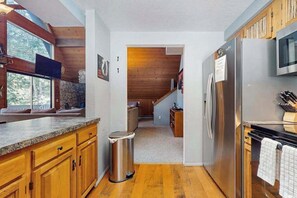 A modern kitchen with wooden cabinets, a stainless steel refrigerator, and a stone fireplace.