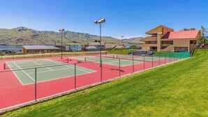 Ein Tennisplatz mit roter und grüner Belag, umzäunt, mit einem Gebäude mit rotem Dach im Hintergrund.