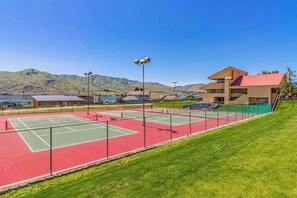 Ein Tennisplatz mit roter und grüner Belag, umzäunt, mit einem Gebäude mit rotem Dach im Hintergrund.