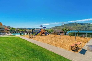A playground with slides and swings, a pool, and a view of hills and water. - Huge 1BR Lakefront 2nd-Floor - Balcony - Pool (Chelan)