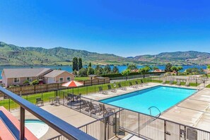 Piscina com espreguiçadeiras e vista para um lago e colinas.