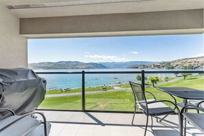 Ein Balkon mit Blick auf einen See und Berge, inklusive Grill und Gartenmöbeln.