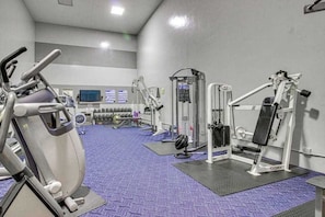 Een sportschool met cardioapparatuur, losse gewichten en een televisiescherm.