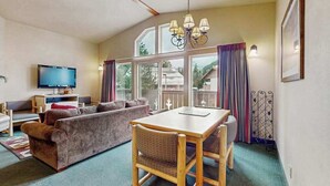 Een gezellige woonkamer met een bank, een eettafel met stoelen, een televisie en grote ramen.