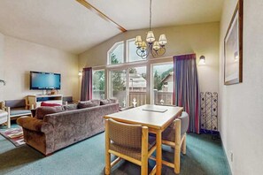 A cozy living room with a sofa, a dining table with chairs, a television, and large windows. - 2 BR condos located in the Icicle Resort (Leavenworth)