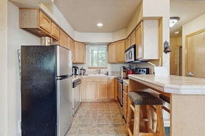 A compact kitchen with wooden cabinets, a black refrigerator, a microwave, and a window providing natural light. - 2 BR condos located in the Icicle Resort (Leavenworth)
