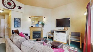 Een woonkamer met een bank, een televisie, een open haard en een spiegel aan de muur.