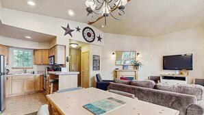 Een moderne keuken met houten kastjes, een eettafel met stoelen, een zithoek met een bank en een flatscreen televisie.
