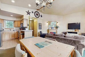 A modern kitchen with wooden cabinets, a dining table with chairs, a living area with a sofa, and a flat-screen TV. - 2 BR condos located in the Icicle Resort (Leavenworth)