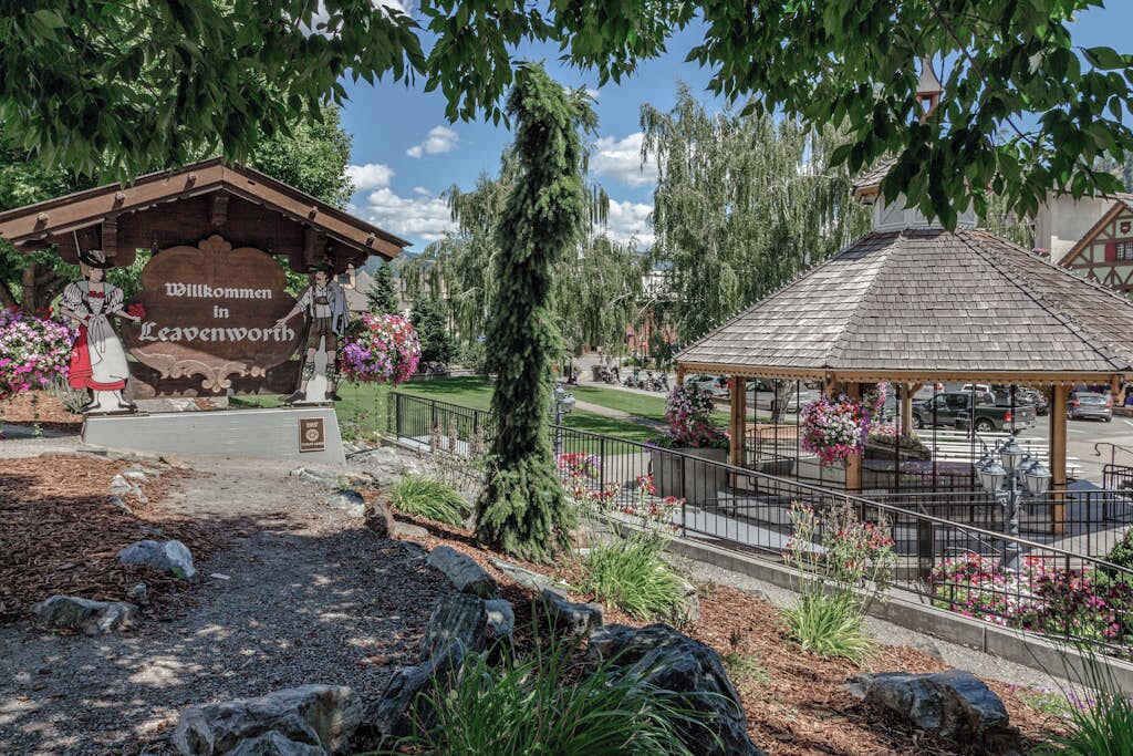 A traditional wooden building with a sign welcoming visitors to Leavenworth, surrounded by a well-maintained garden with flowering plants and a gazebo.