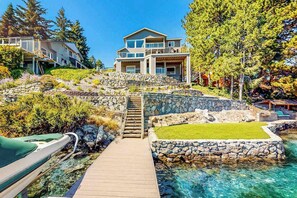 Ein Küstenanwesen mit einer Holzterrasse, die zu einer Steintreppe führt, einem klaren, blauen Pool und einem zweistöckigen Haus mit Balkon.