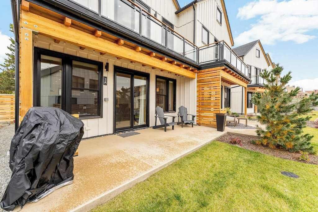 A modern house with a covered patio, outdoor seating, and a small tree.