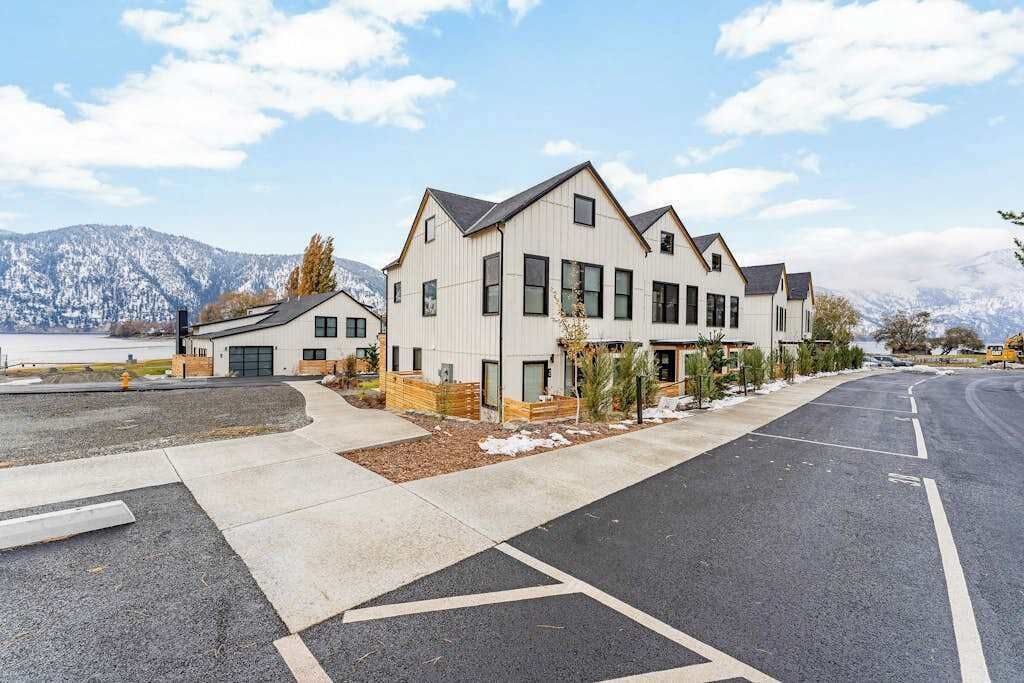A modern multi-story residential building with a garage, a driveway, and a clear view of a snowy mountain range in the background.