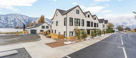 A modern multi-story residential building with a garage, a driveway, and a clear view of a snowy mountain range in the background.