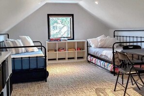 Ein kompaktes Zimmer mit Hochbett, Schreibtisch und Stuhl. Ein Fenster bietet Blick auf Bäume, und ein Regal beherbergt Bücher und Kartons.