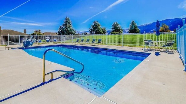 A rectangular swimming pool with a metal ladder, surrounded by a white fence, with chairs and umbrellas on the right side. - Modern 3BR Lakeview - Pool - Dock - Fireplace (Manson)