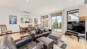 A modern living room with a sectional sofa, a dining table with chairs, and a television. - Modern 3BR Lakeview - Pool - Dock - Fireplace (Manson)