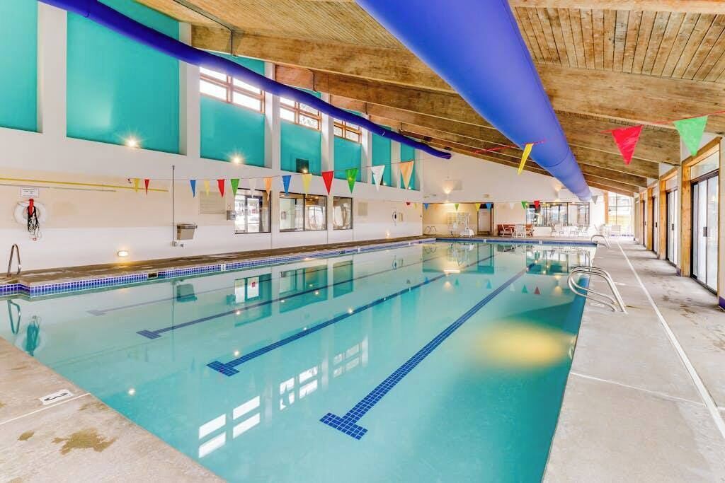 An indoor swimming pool with clear lane markings, a wooden ceiling, and colorful flags.