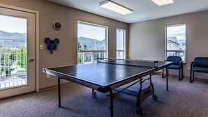Ein Zimmer mit einer Tischtennisplatte, zwei Fenstern und einer Tür.