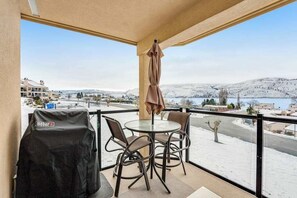 A balcony with a table and chairs, a grill, and a view of a snowy landscape. - 1BR Lakeview 2nd-Floor - Balcony - Pool (Chelan)