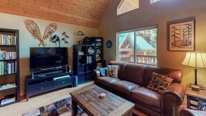 A cozy living room with a wooden ceiling, a leather sofa, a television, and a bookshelf. - Secluded 3BR Mountainview - Hot Tub - WoodStove (Leavenworth)