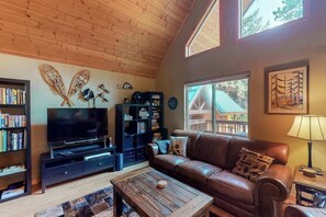 A cozy living room with a wooden ceiling, a leather sofa, a television, and a bookshelf. - Secluded 3BR Mountainview - Hot Tub - WoodStove (Leavenworth)