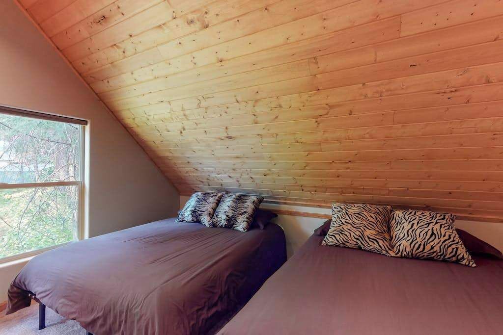 Une chambre avec deux lits, un plafond en pente et une fenêtre.