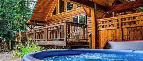 A wooden cabin with a hot tub, deck, and multiple windows.