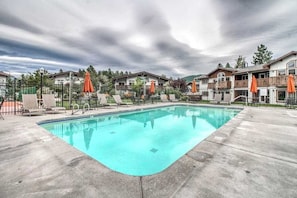 A swimming pool with lounge chairs and umbrellas, surrounded by buildings with balconies. - 1 BR condo located in Icicle Village, Leavenworth (Leavenworth)