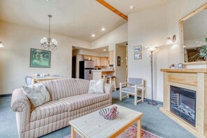 Ein Wohnzimmer mit Sofa, Couchtisch und Kamin. Im Hintergrund ist eine Küche zu sehen.
