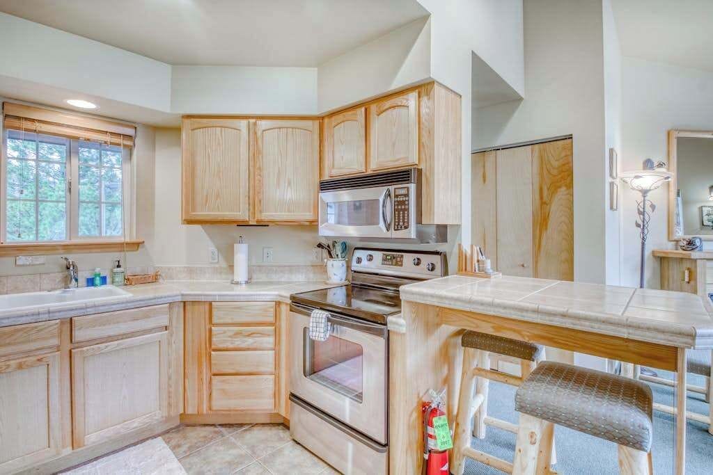 A kitchen with wooden cabinets, a microwave, an oven, and a dining area with a bench.